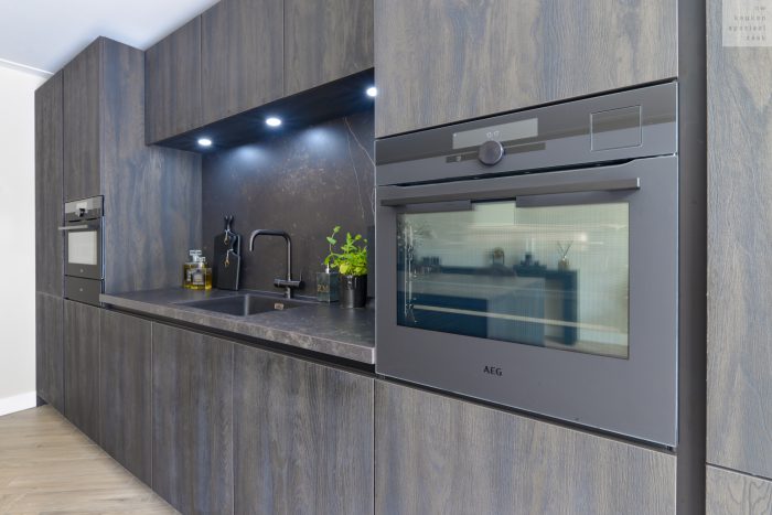 Strak moderne keuken met verlichte nis, in donkere tinten